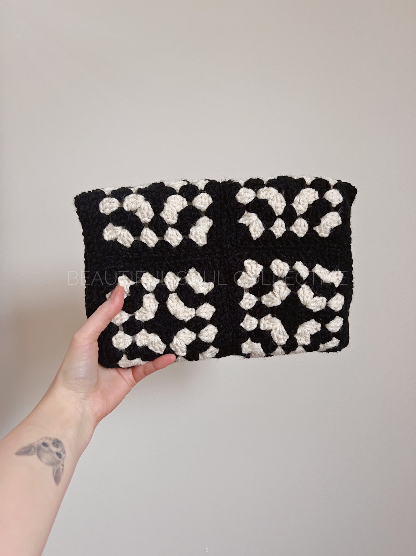 Black and white crochet e-reader sleeve held by a hand against a plain background