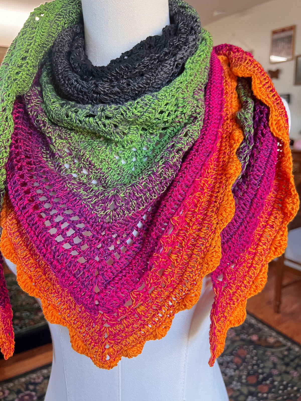 Crochet scarf on a mannequin in a gradient from black, grey, green, pink to orange