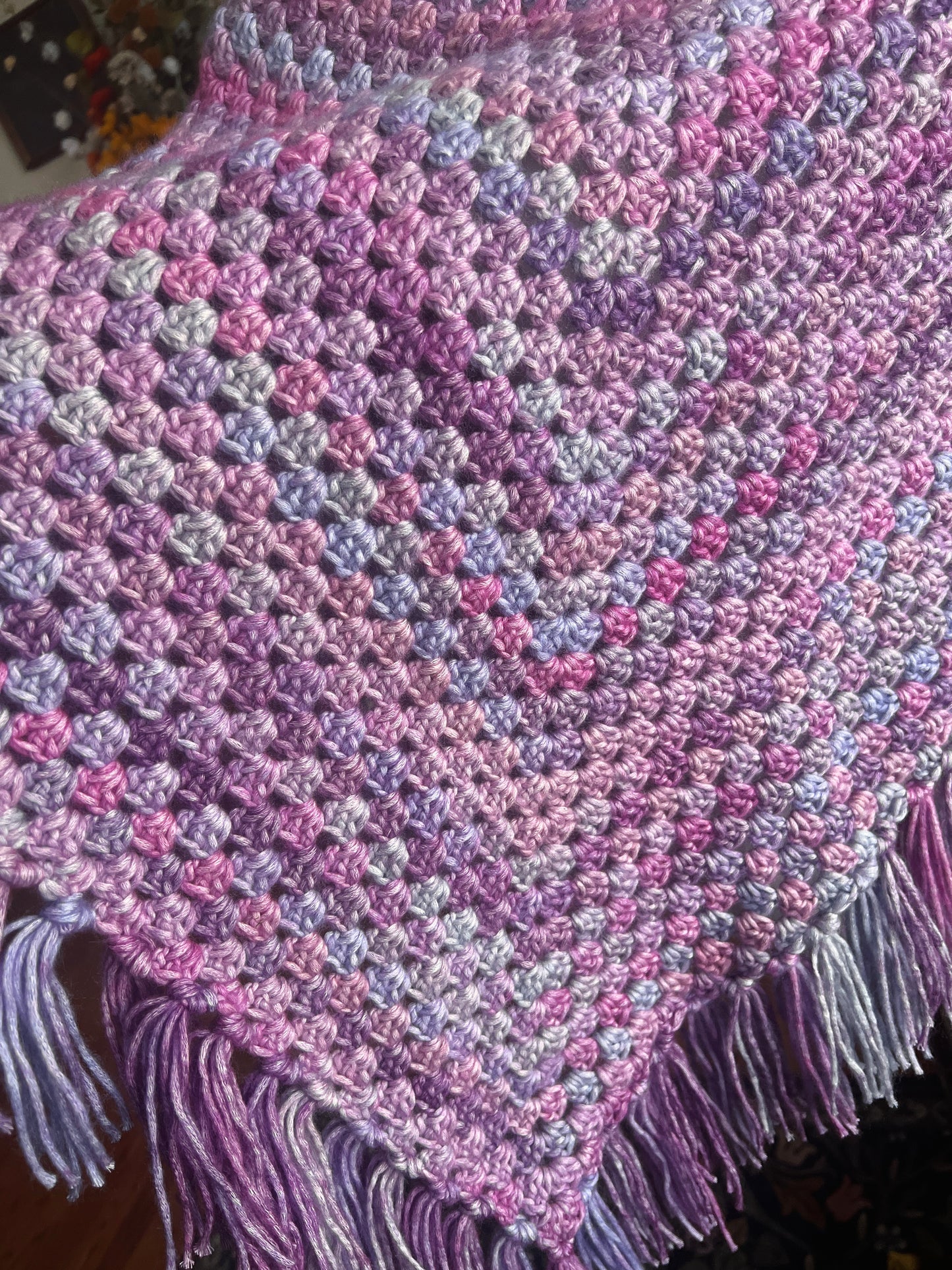 Crocheted poncho in pink, purple, and blue on a dark background.