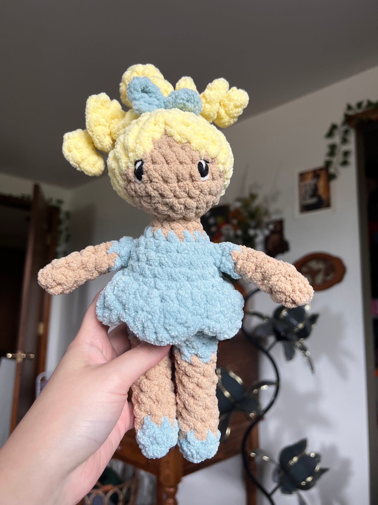 Crochet doll with beige skin and blonde hair. Blue bow, dress and shoes. The eyes are embroidered.