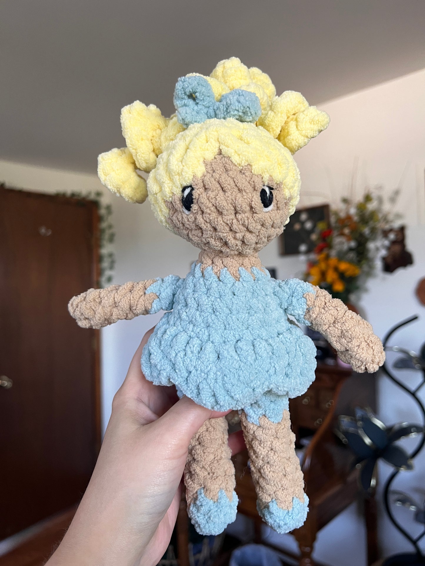 Crochet doll with beige skin and blonde hair. Blue bow, dress and shoes. The eyes are embroidered.