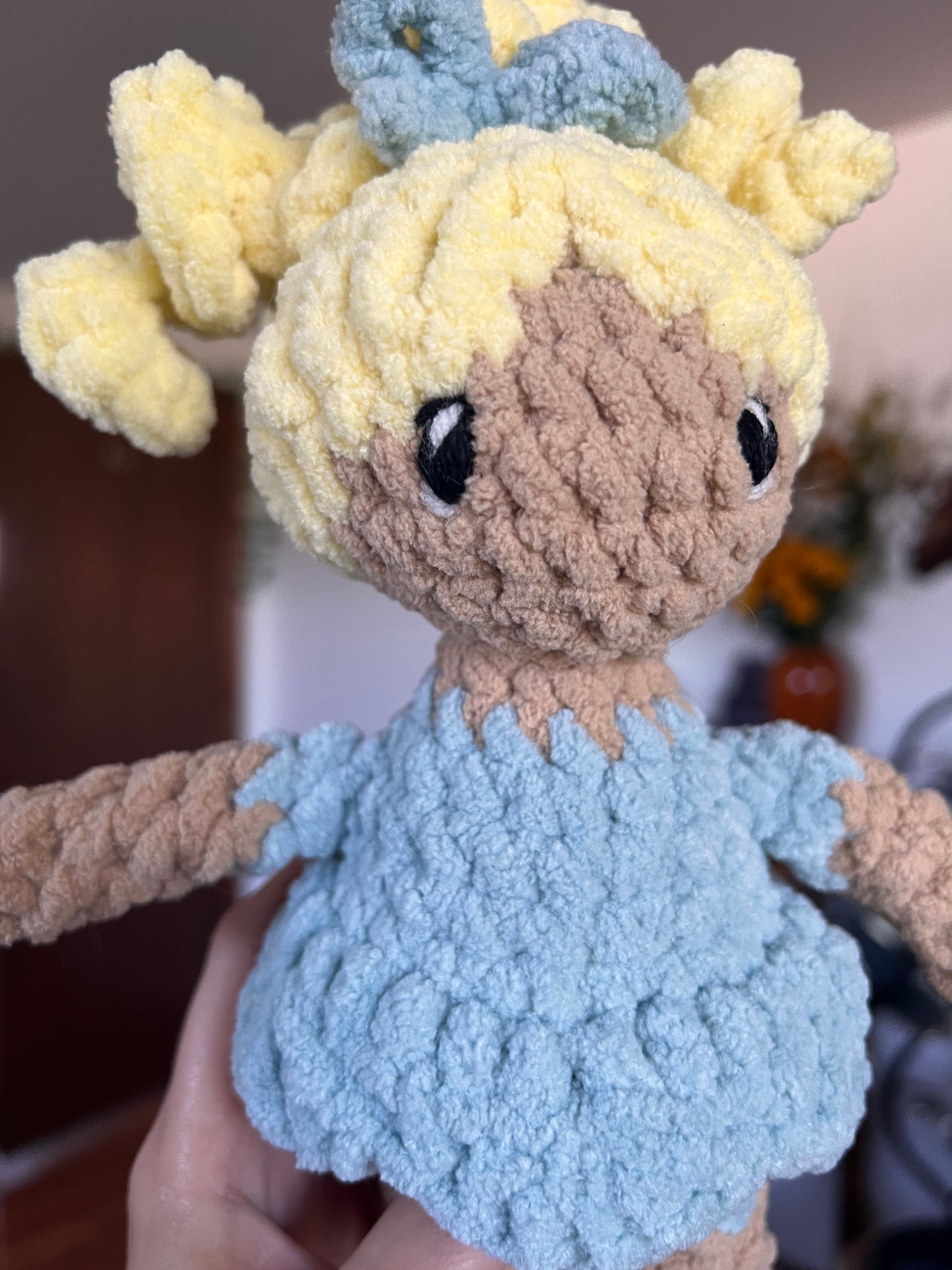Crochet doll with beige skin and blonde hair. Blue bow, dress and shoes. The eyes are embroidered.