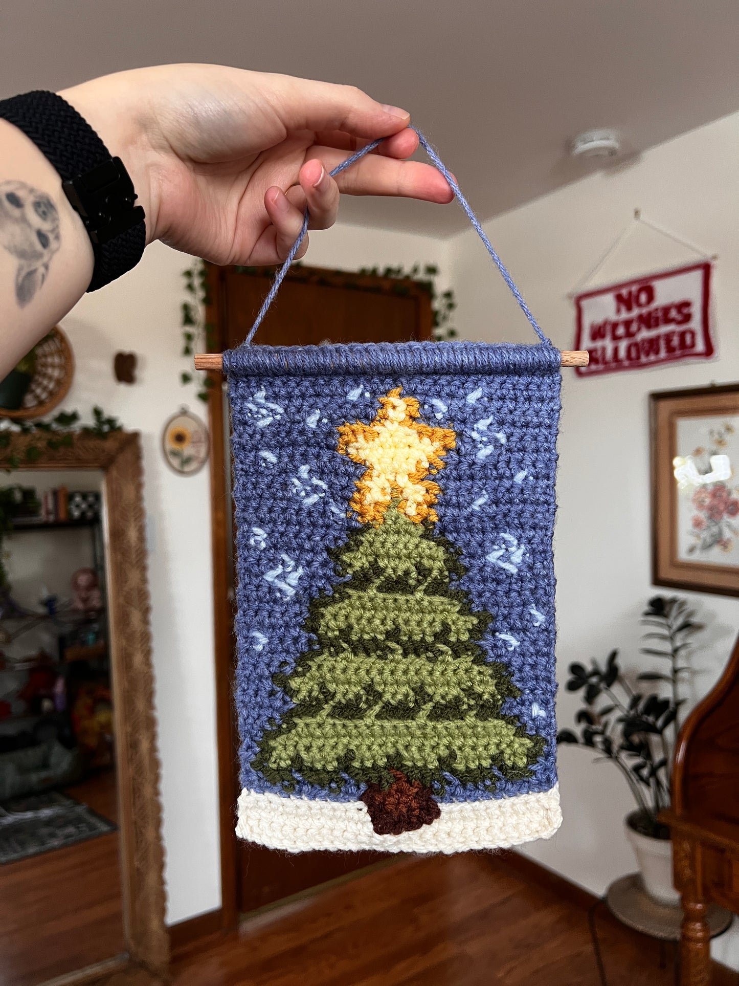 Hand holding a small crocheted Christmas-themed tapestry with a tree and star design.