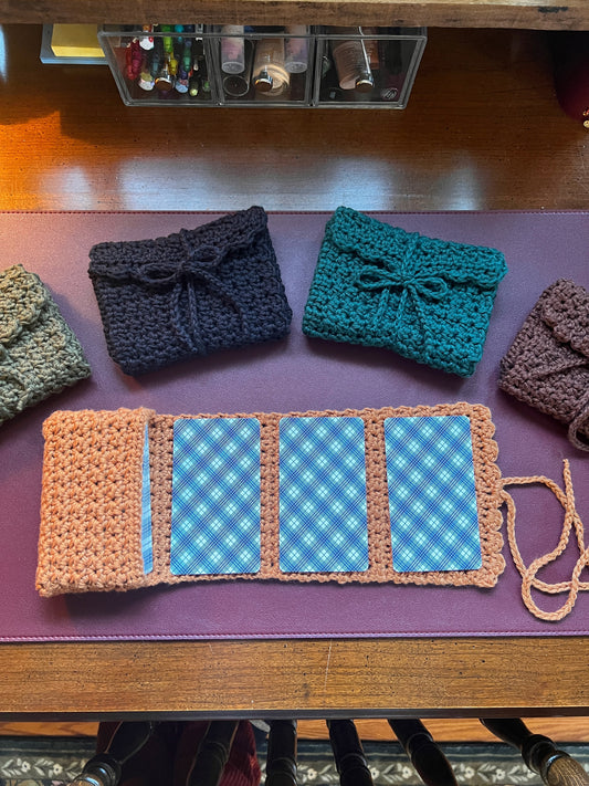 Three crocheted pouches in black, blue, and brown on a purple surface with a checkered pattern.