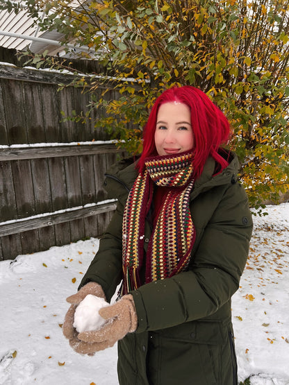 Person with red hair holding a snowball outdoors in winter showcasing a handmade crochet scarf