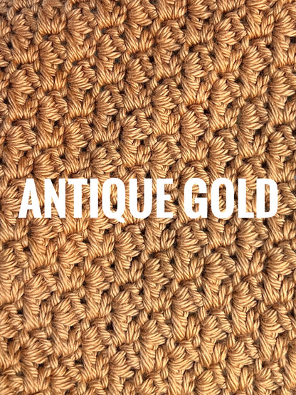A close-up of a textured crochet washcloth swatch in a warm antique gold color, with the words 'ANTIQUE GOLD' overlaid in large white text across the center.