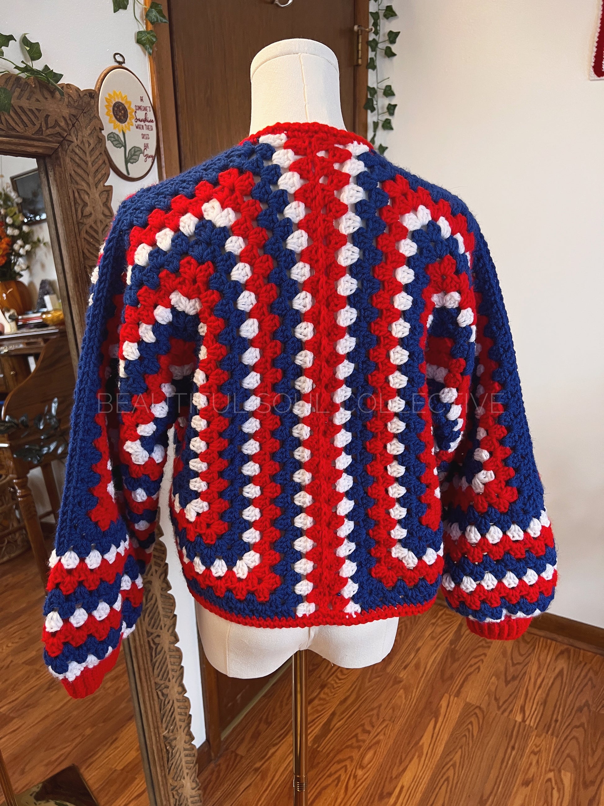 Mannequin wearing a colorful crochet sweater with red, blue, and white pattern in a home setting.
