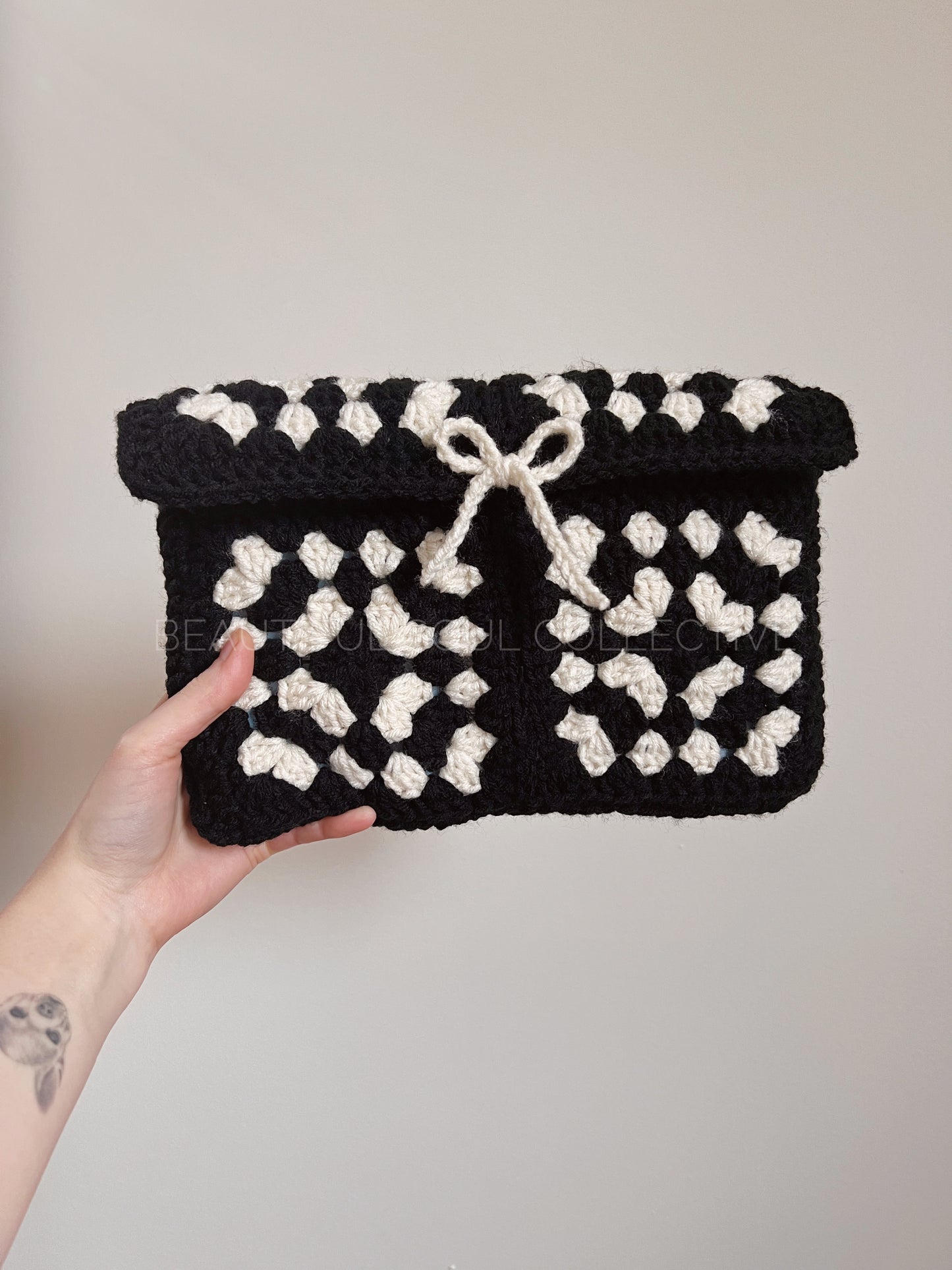 Black and white crochet granny square e-reader sleeve held by a hand against a plain background
