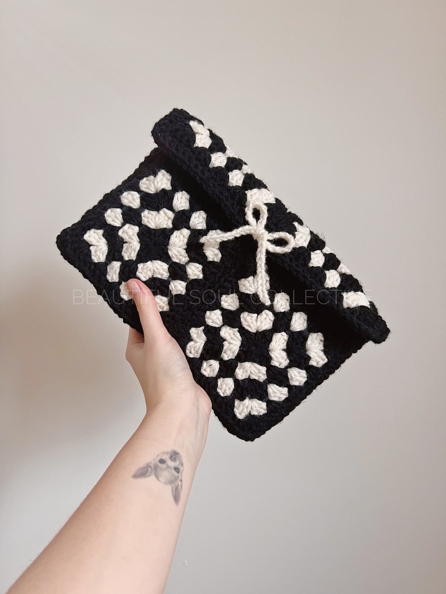 Black and white crochet book pouch held by a hand against a neutral background