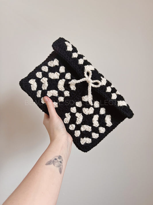 Black and white crochet book pouch held by a hand against a neutral background