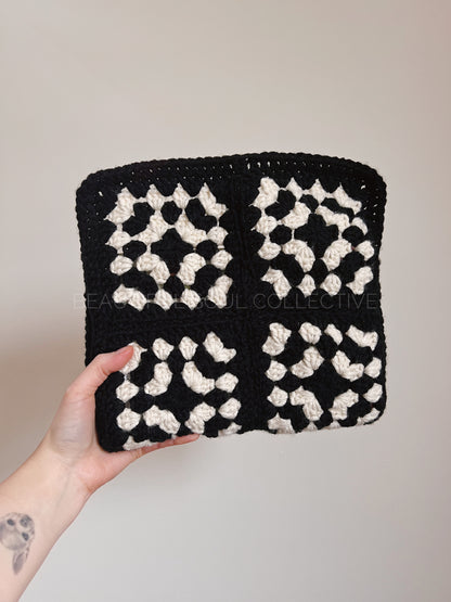 Hand holding a black and white granny square book sleeve against a neutral background