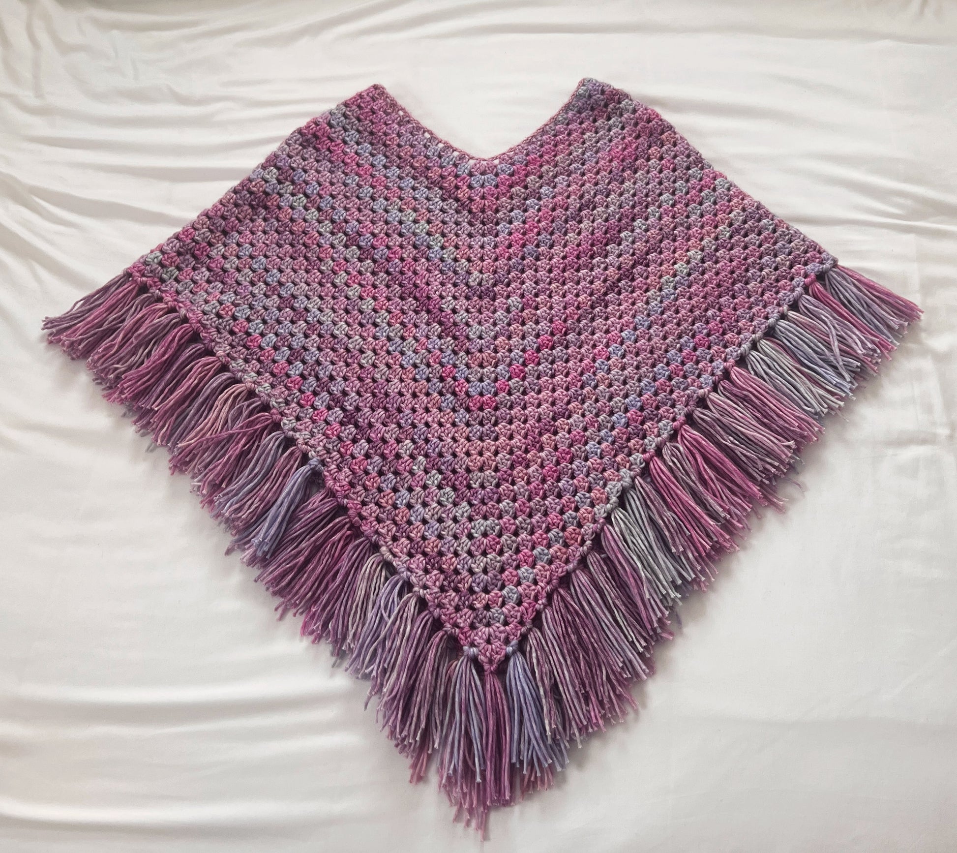Purple, pink and blue crochet poncho with fringe on a white surface