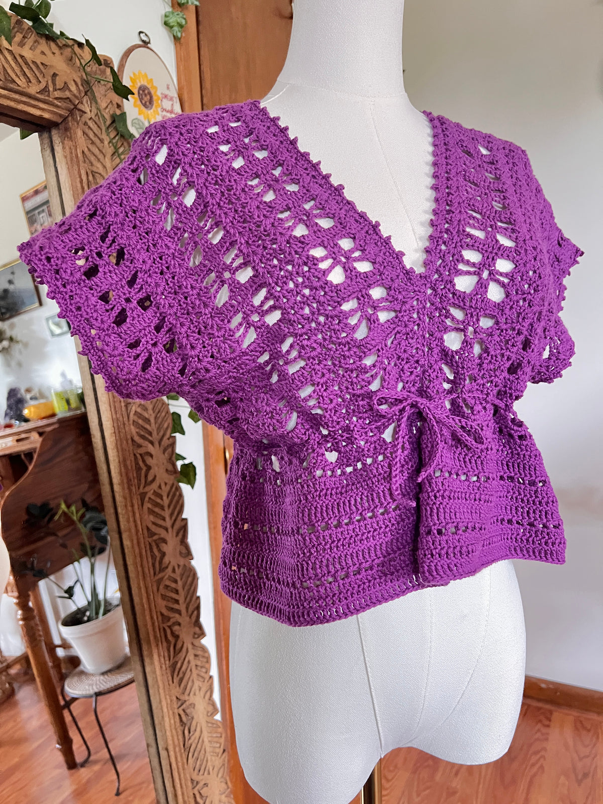 A purple crochet short sleeve top on a mannequin in front of a wooden mirror
