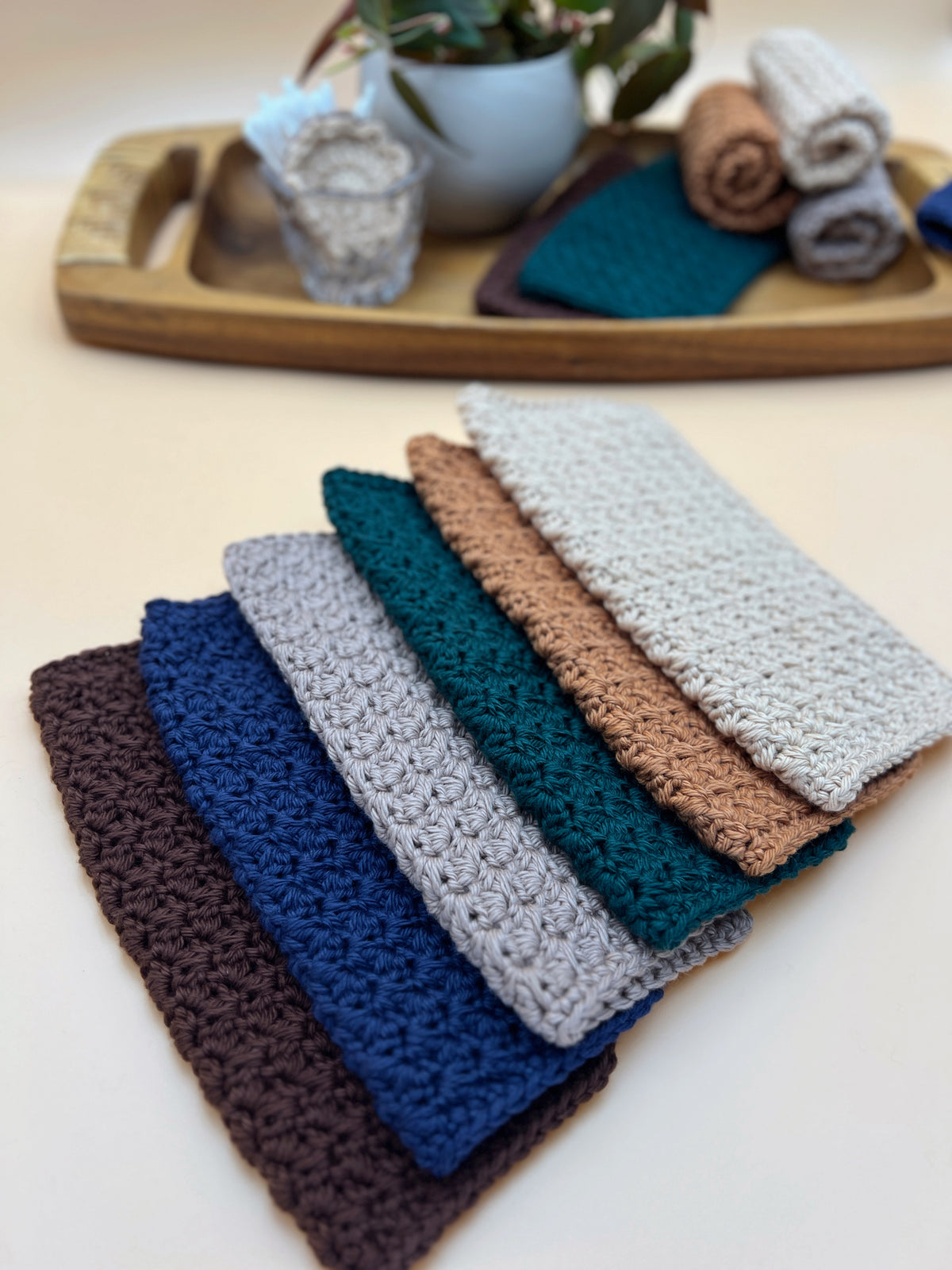 Six crochet washcloths layed flat with a tray in the background containing decor and additional washcloths