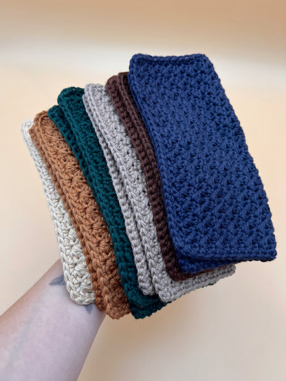 Six crochet washcloths held by a person in tan, orange, teal, taupe, brown and navy blue