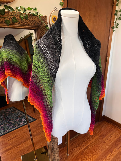 Crochet shawl in a gradient of black, grey, green, pink and orange on a mannequin in front of a mirror