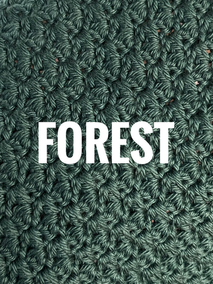 A close-up of a textured crochet washcloth swatch in a deep green color, with the words 'FOREST' overlaid in large white text across the center.