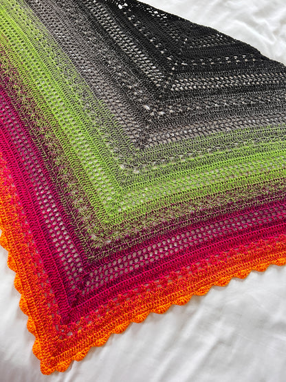 Crochet shawl in a gradient of black, grey, green, pink and orange laid flat on a white background
