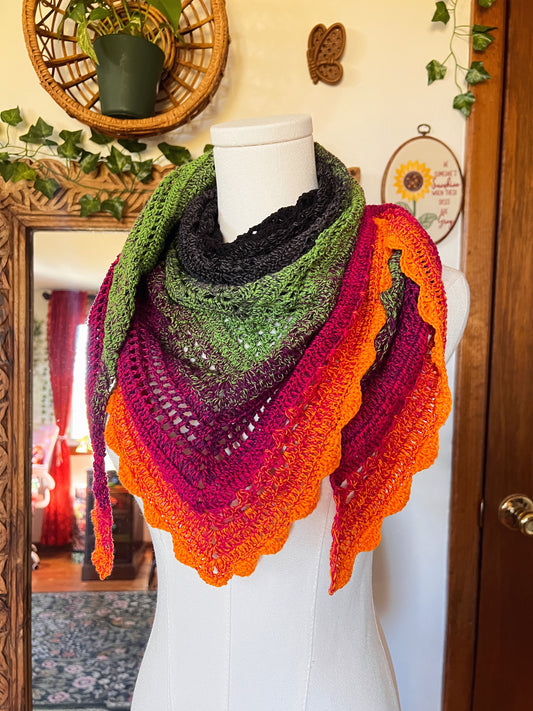 Crochet scarf in a gradient of black, grey, green, pink and orange on a mannequin in front of a mirror and decor.