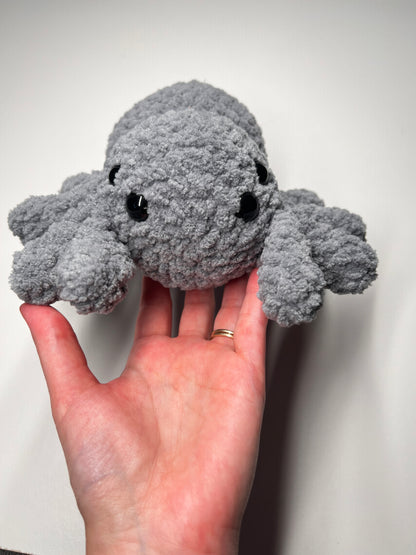 Hand holding a gray plush spider toy against a plain background