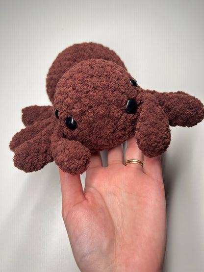Small brown plush spider toy held in a hand against a plain background