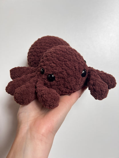 Brown plush spider toy held in a hand against a plain background