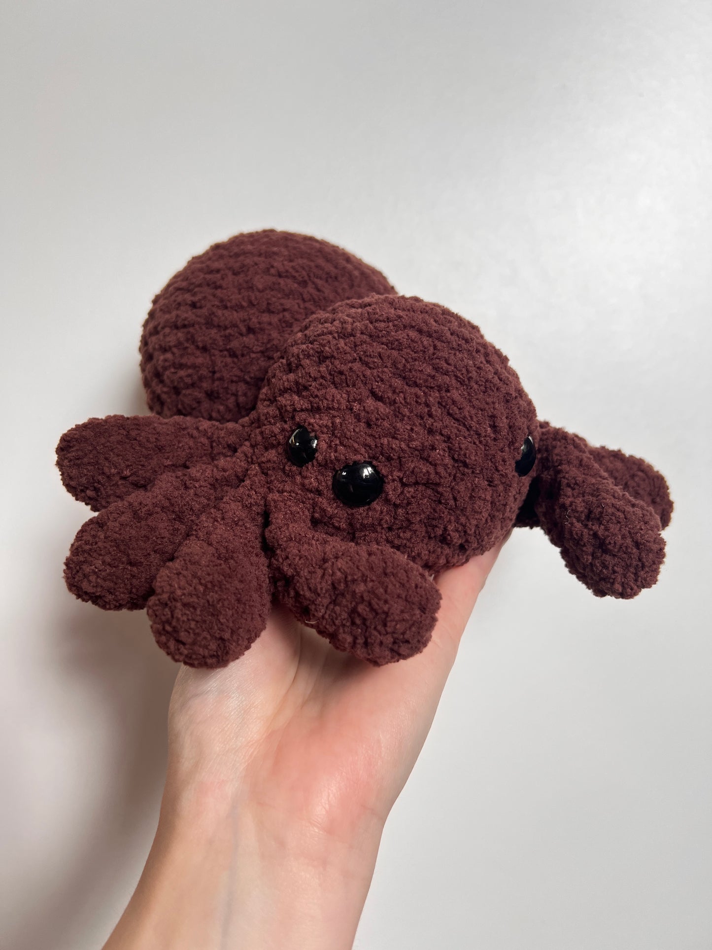 Brown plush spider toy held in a hand against a white background