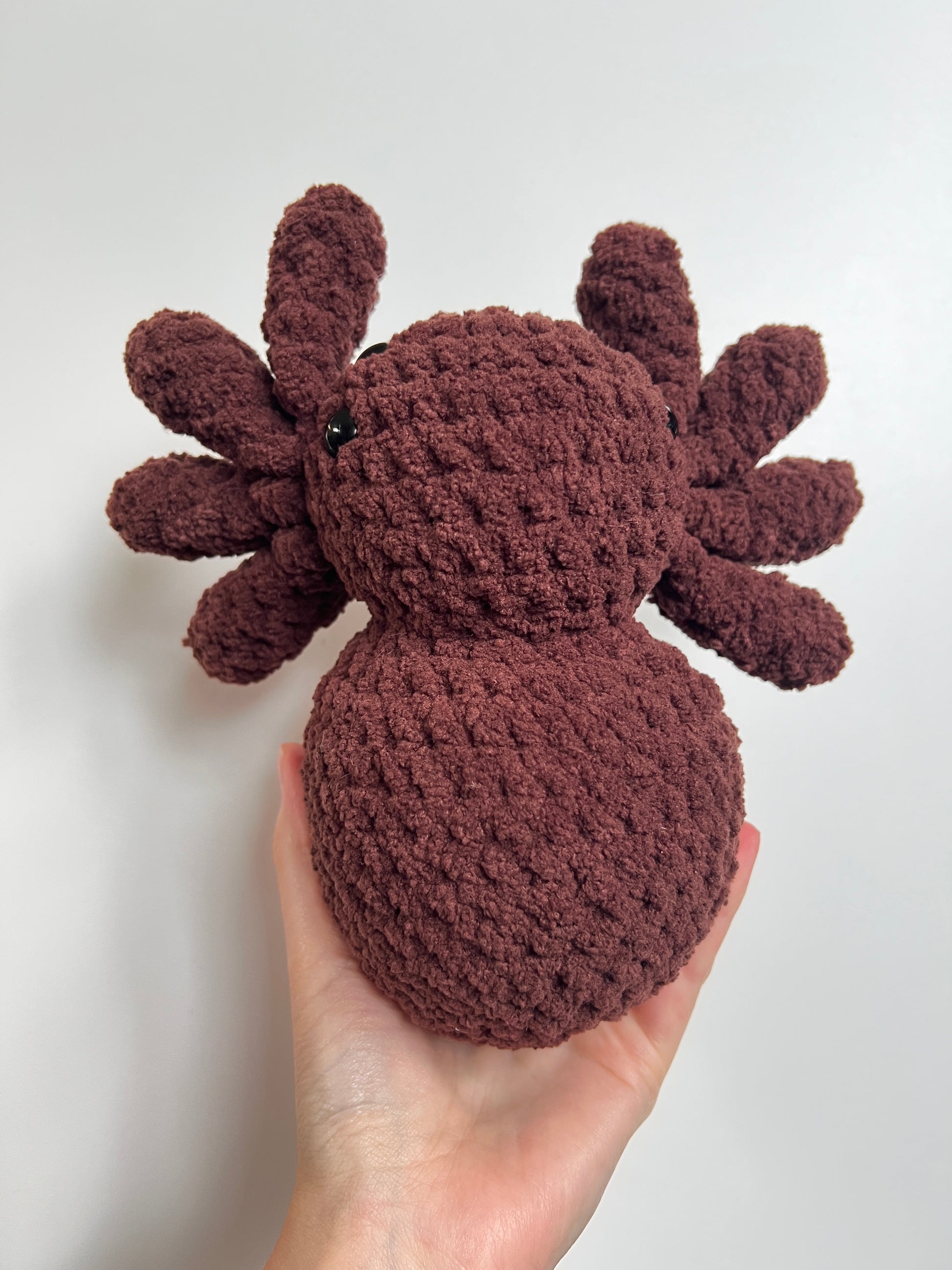 Hand holding a brown crochet spider toy against a white background