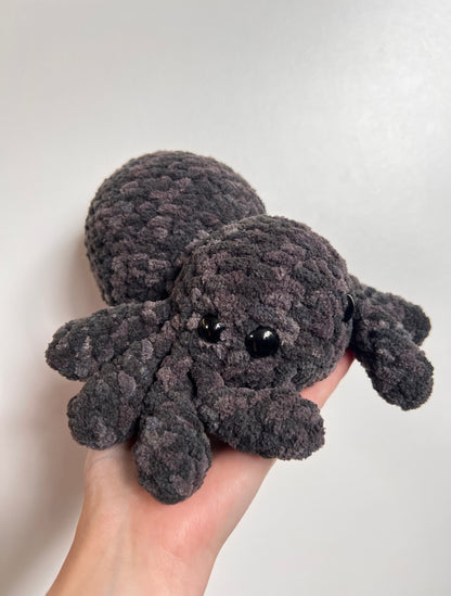 Gray crochet spider held in a hand against a white background