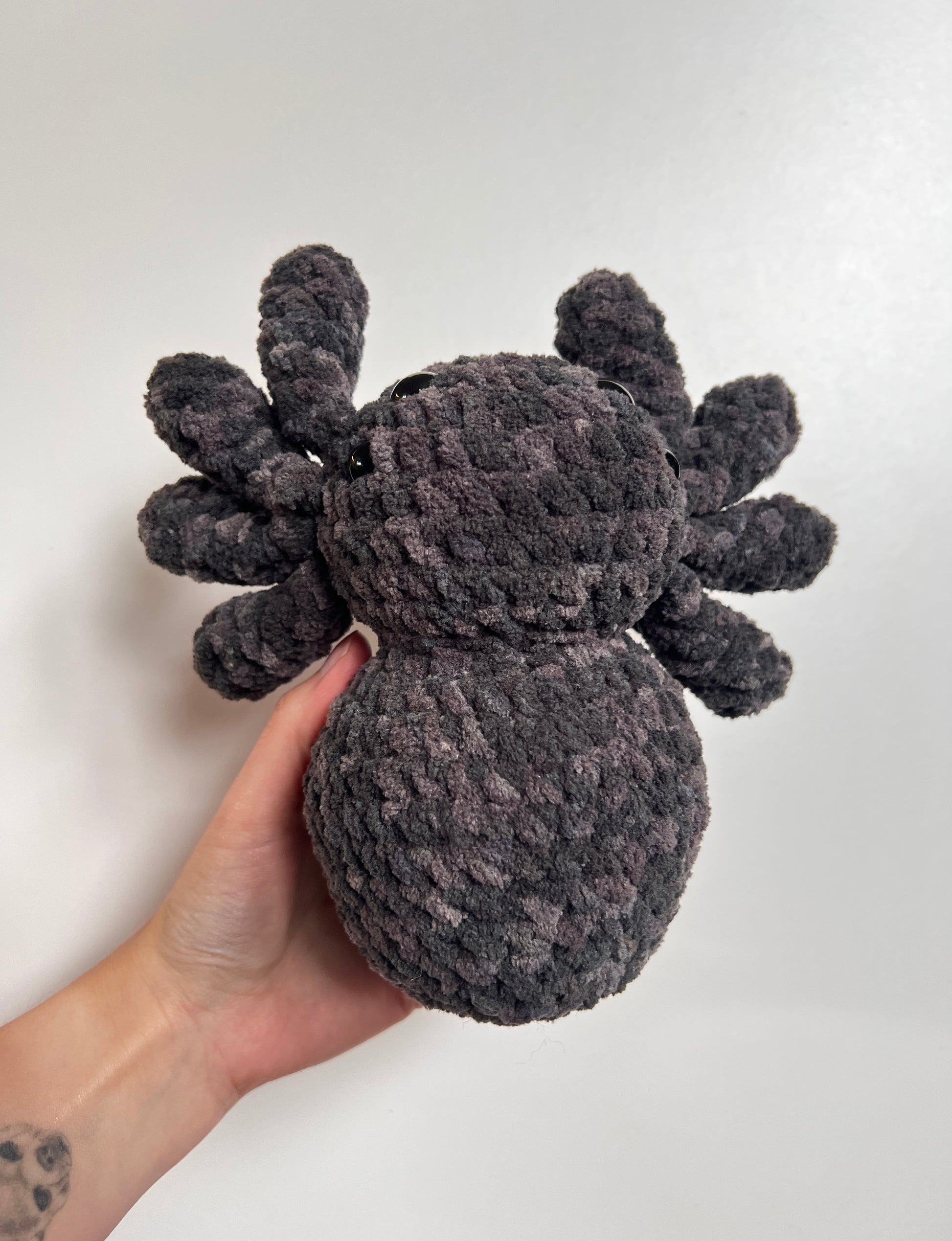 Hand holding a plush spider toy against a plain background