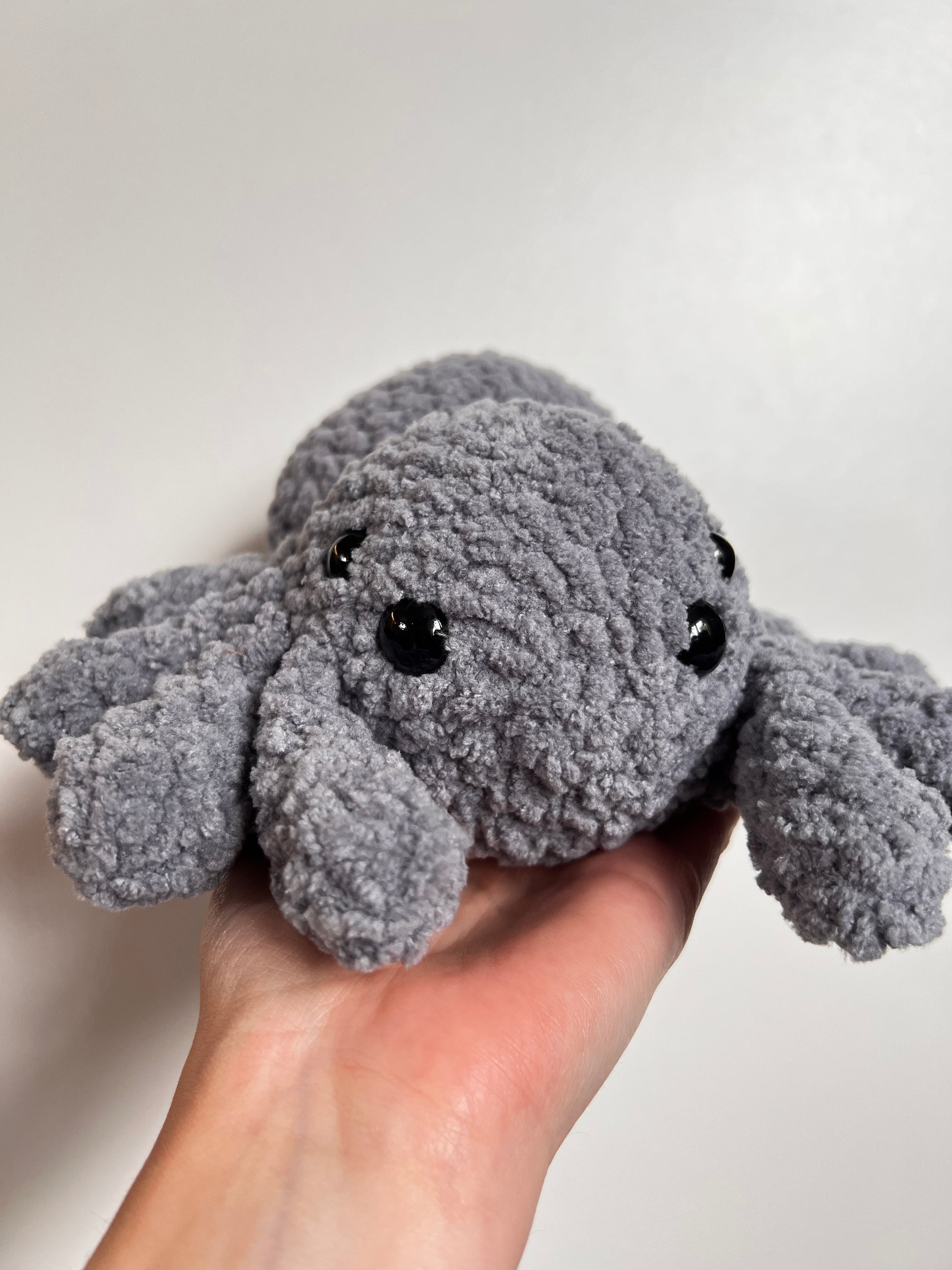 Gray plush toy resembling a spider held by a hand against a plain background