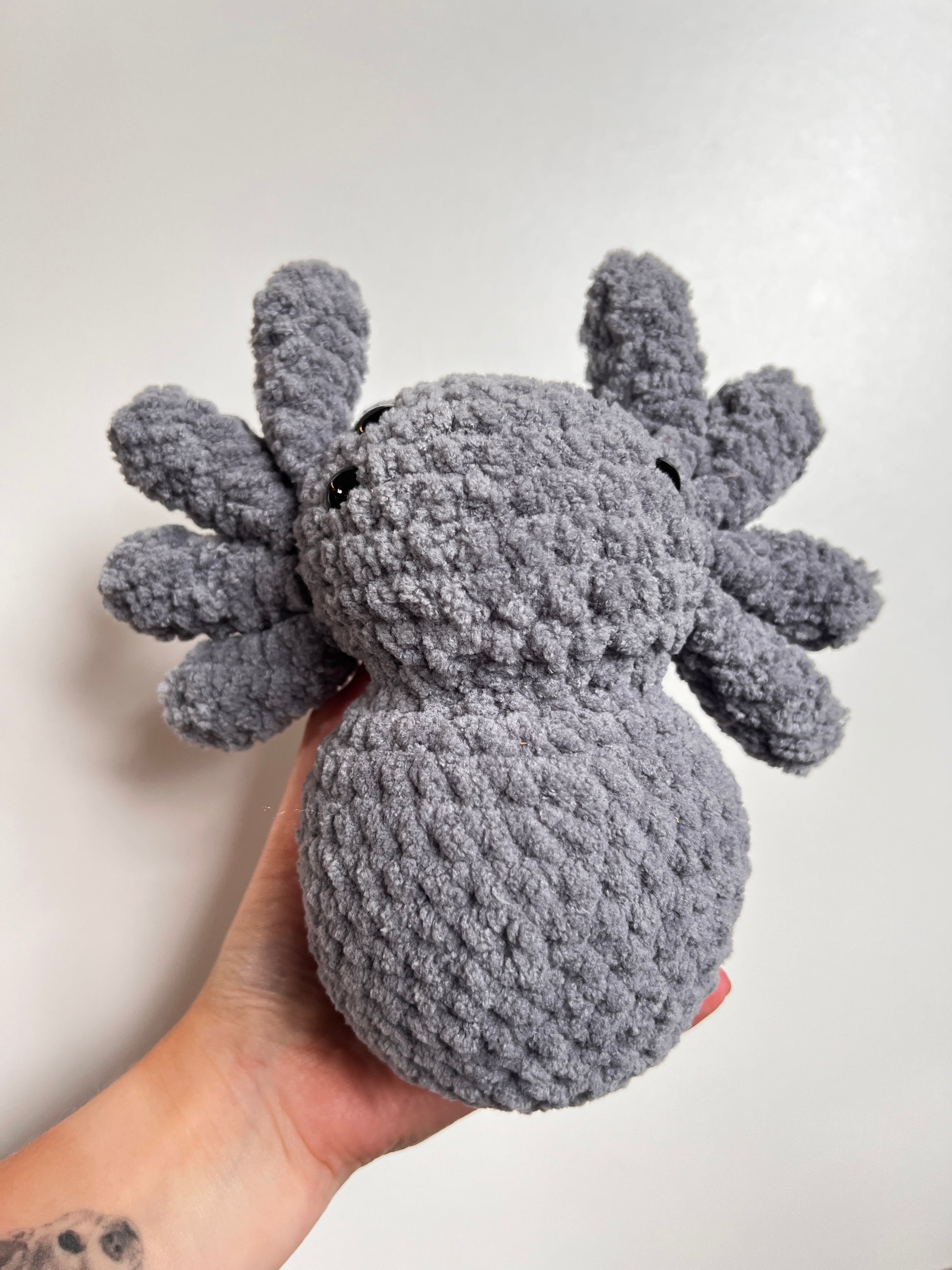 Hand holding a gray plush spider toy against a white background