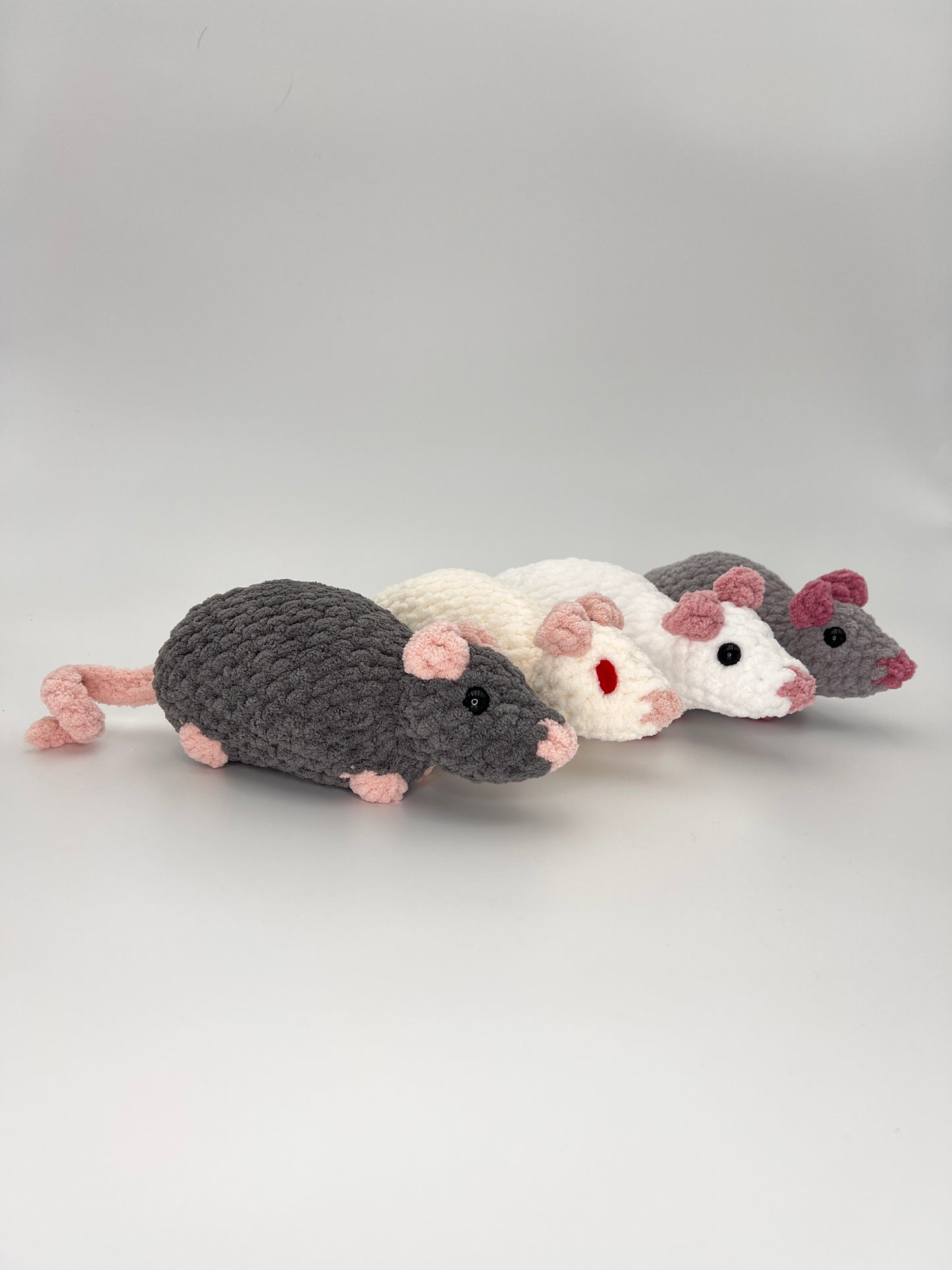 Four crocheted rat/mouse toys in gray, white, and pink on a light gray background