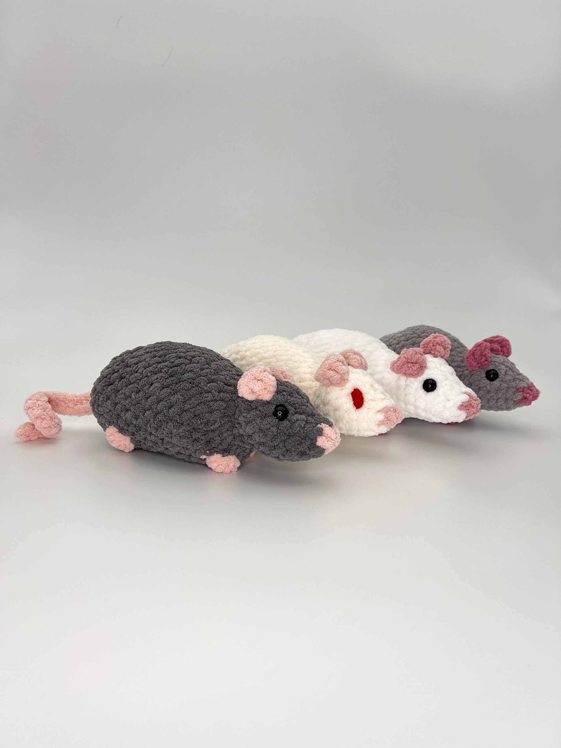 Four crocheted rat/mouse toys in gray, white, and pink on a light gray background