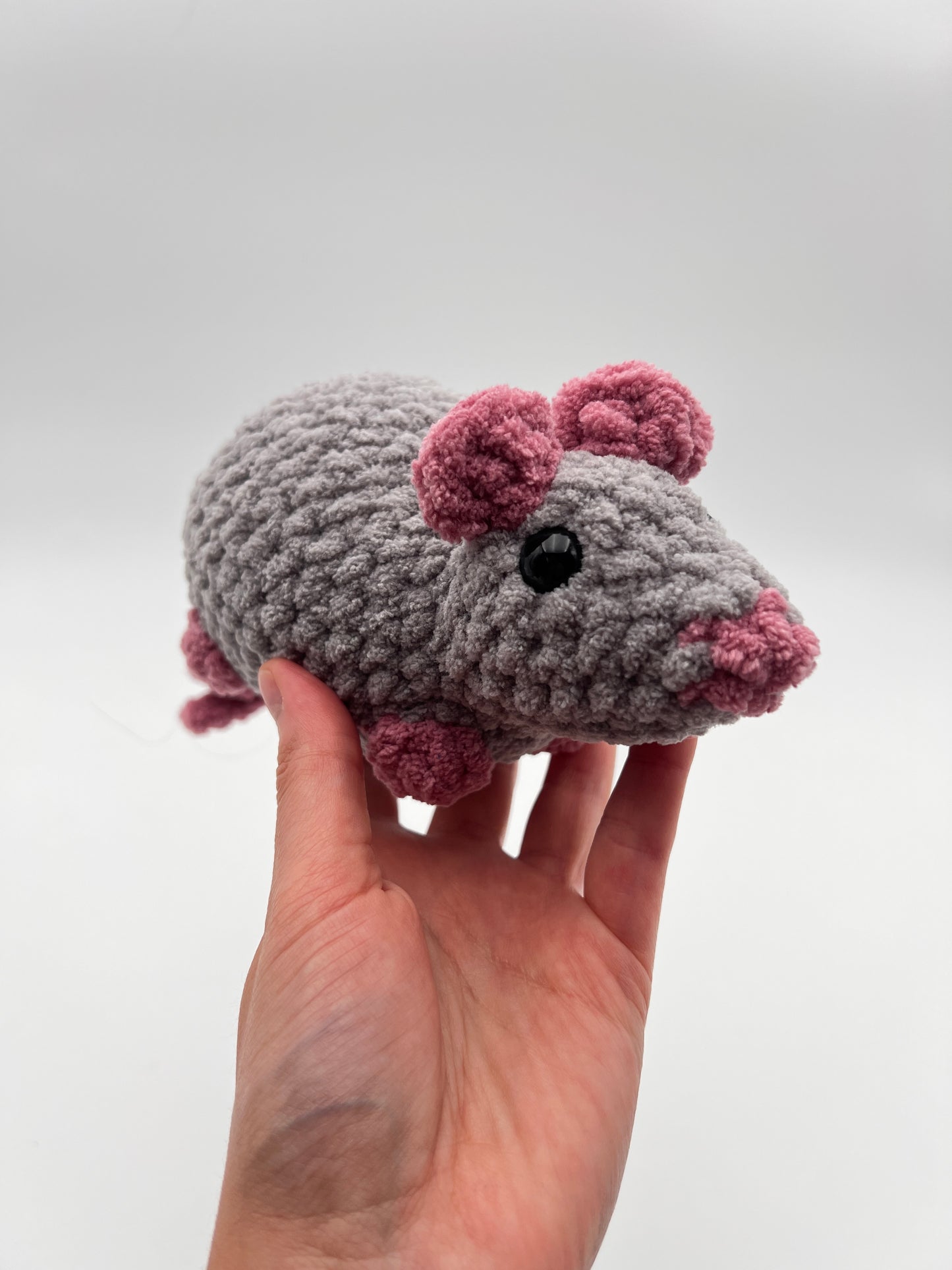 Hand holding a small crocheted animal toy with pink accents on a white background