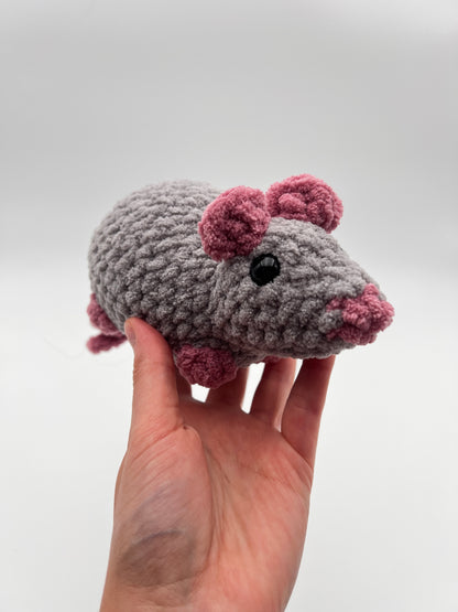 Hand holding a small crocheted animal toy with pink accents on a white background