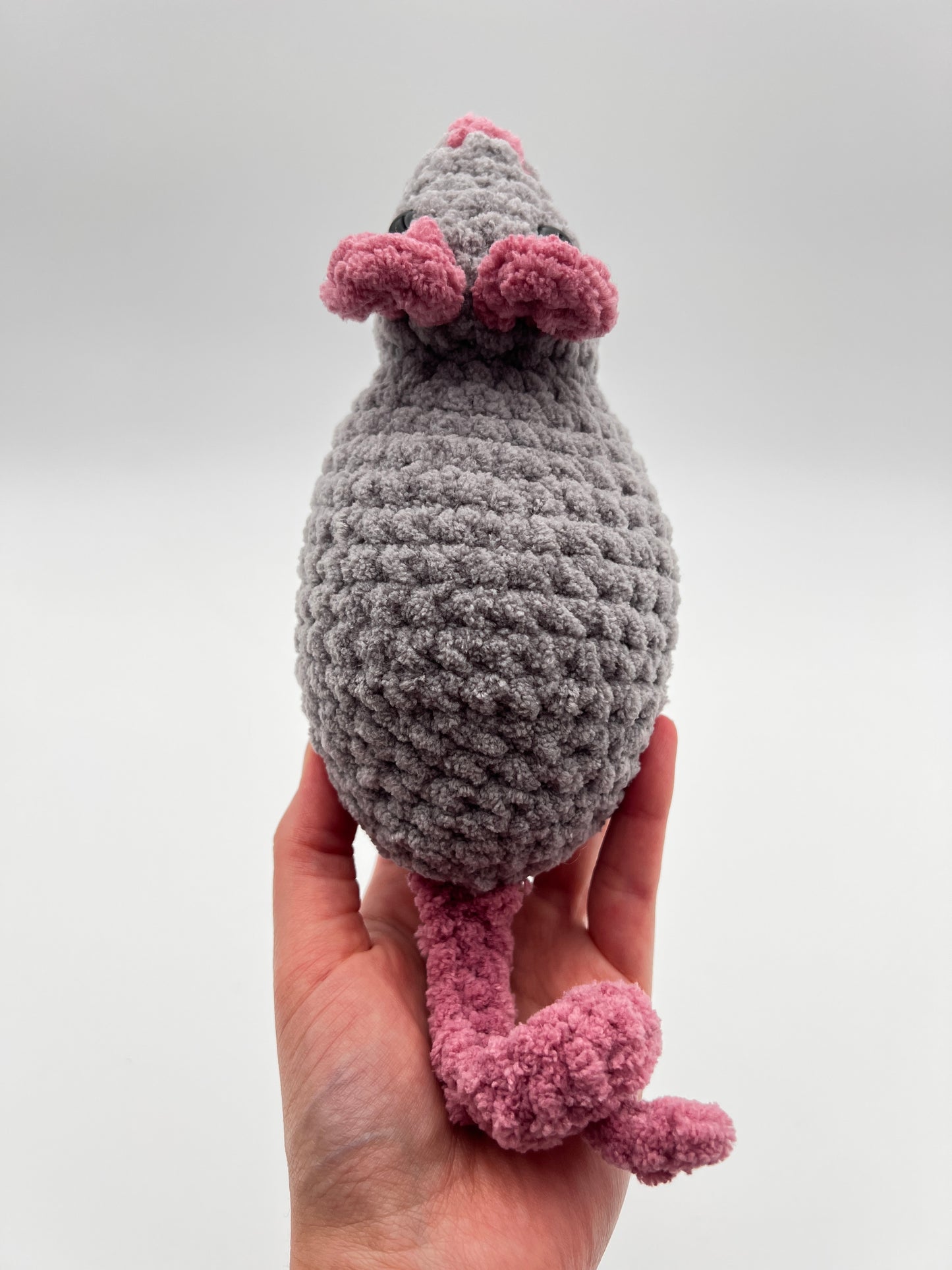 Hand holding a gray and pink crochet rat toy against a white background