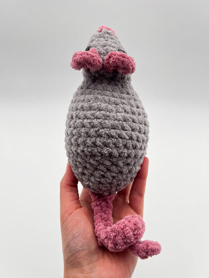 Hand holding a gray and pink crochet rat toy against a white background