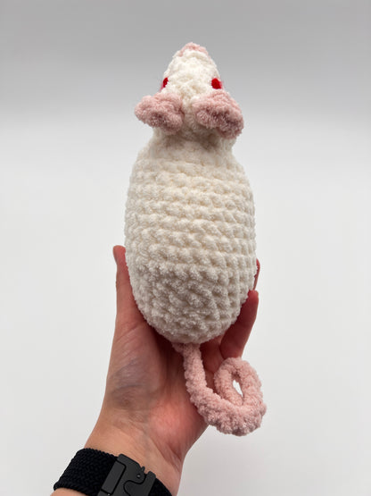 Hand holding a white and pink crochet rat toy with red eyes against a plain background