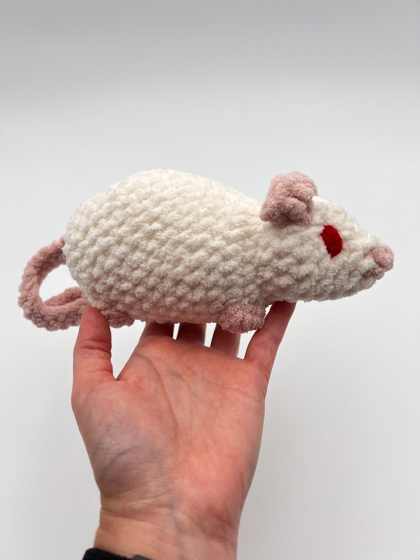 Hand holding a white and pink rat toy with red eyes
