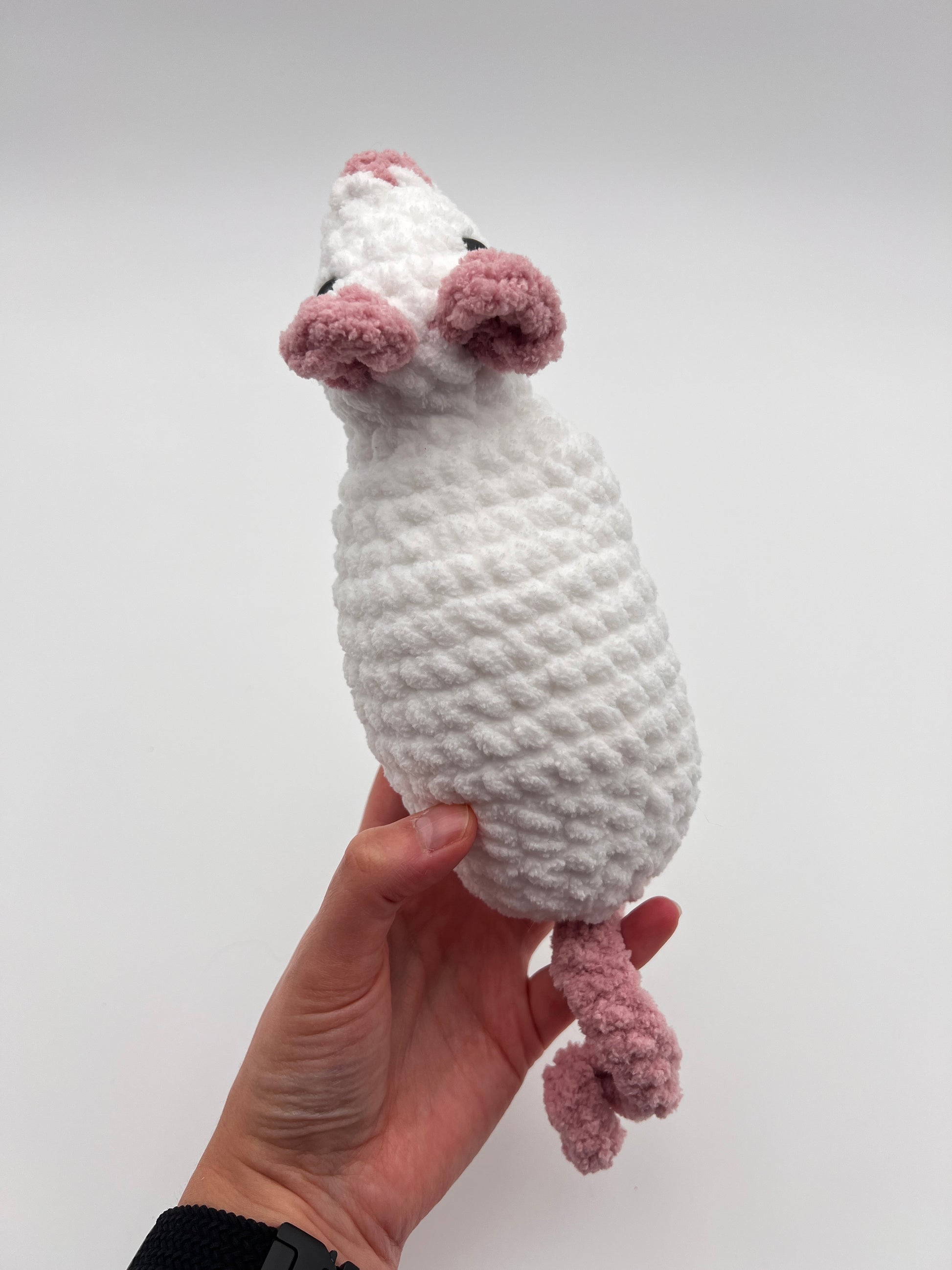 Hat holding white and pink rat toy crochet pushie against a white background