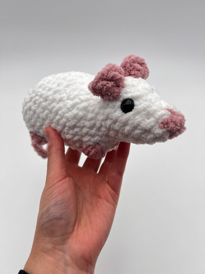 Hand holding a small white and pink crochet mouse toy against a plain background