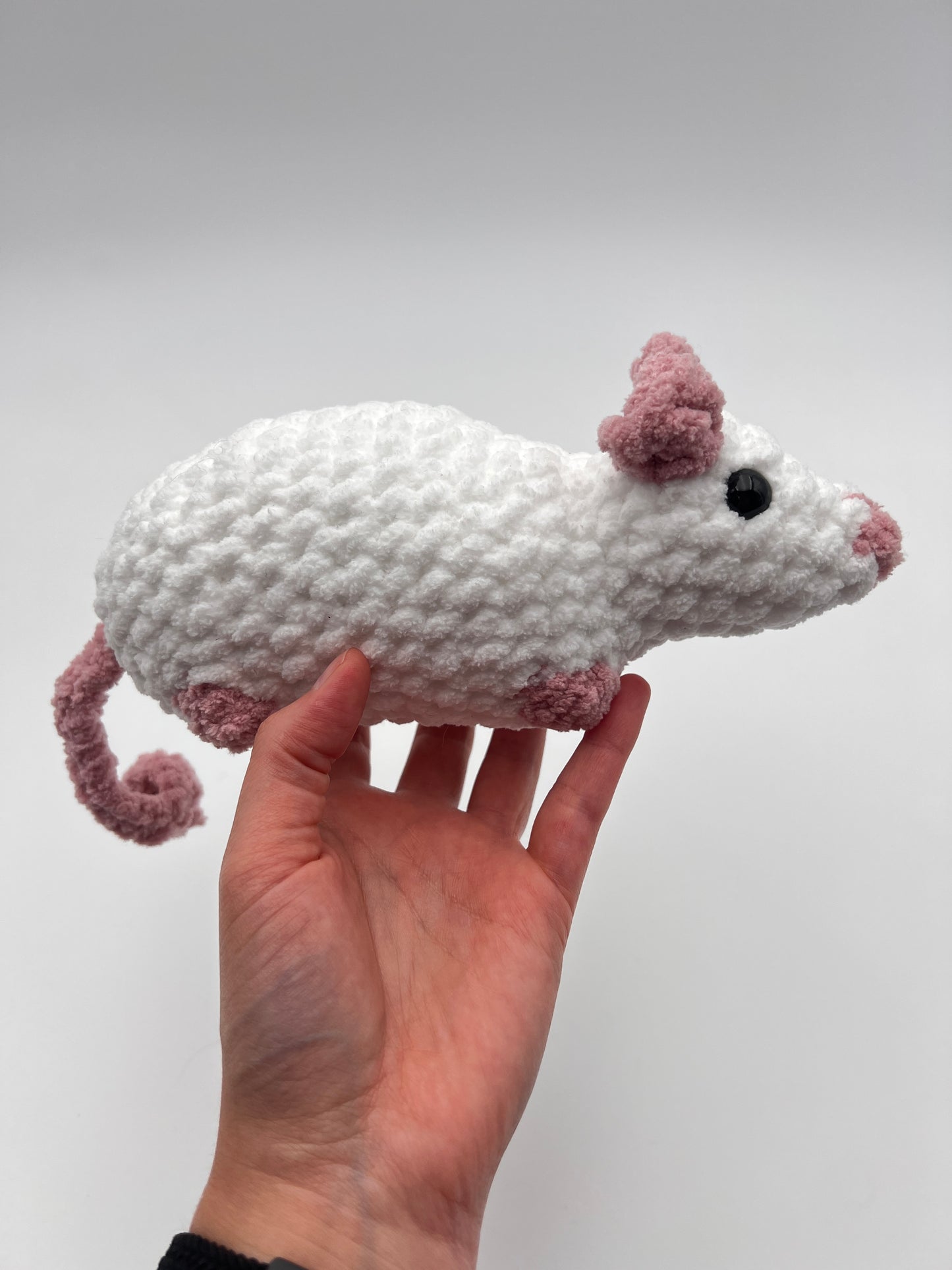 Hand holding a crochet rat stuffed animal against a plain background
