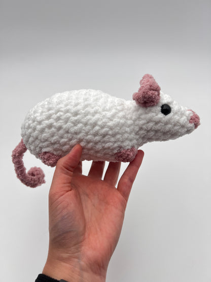 Hand holding a crochet rat stuffed animal against a plain background