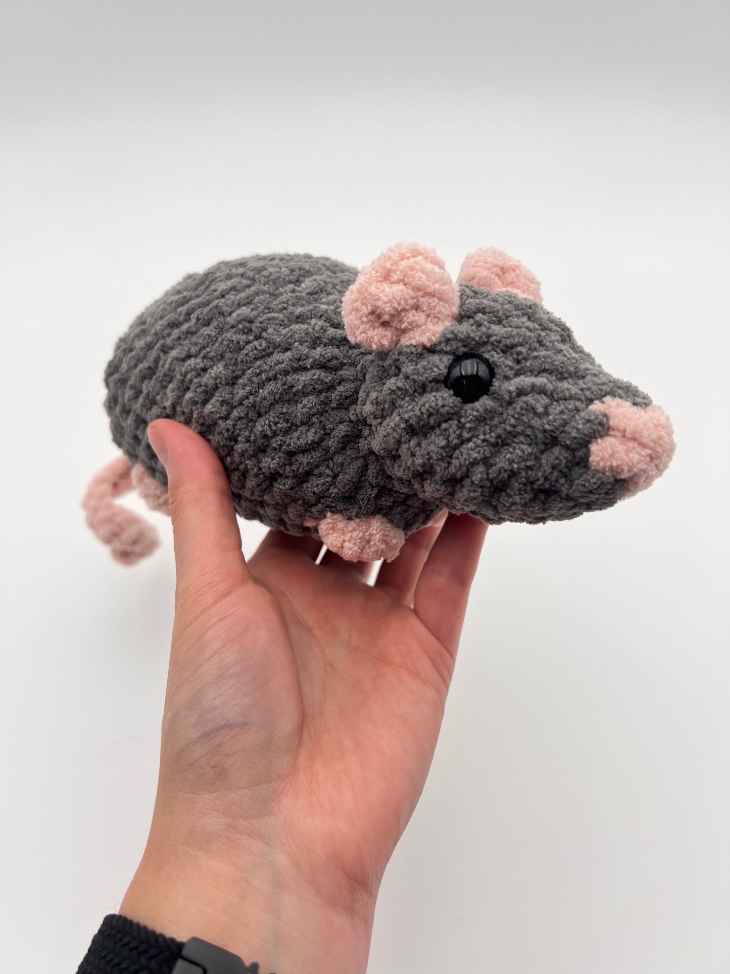Hand holding a gray mouse stuffed animal against a white background