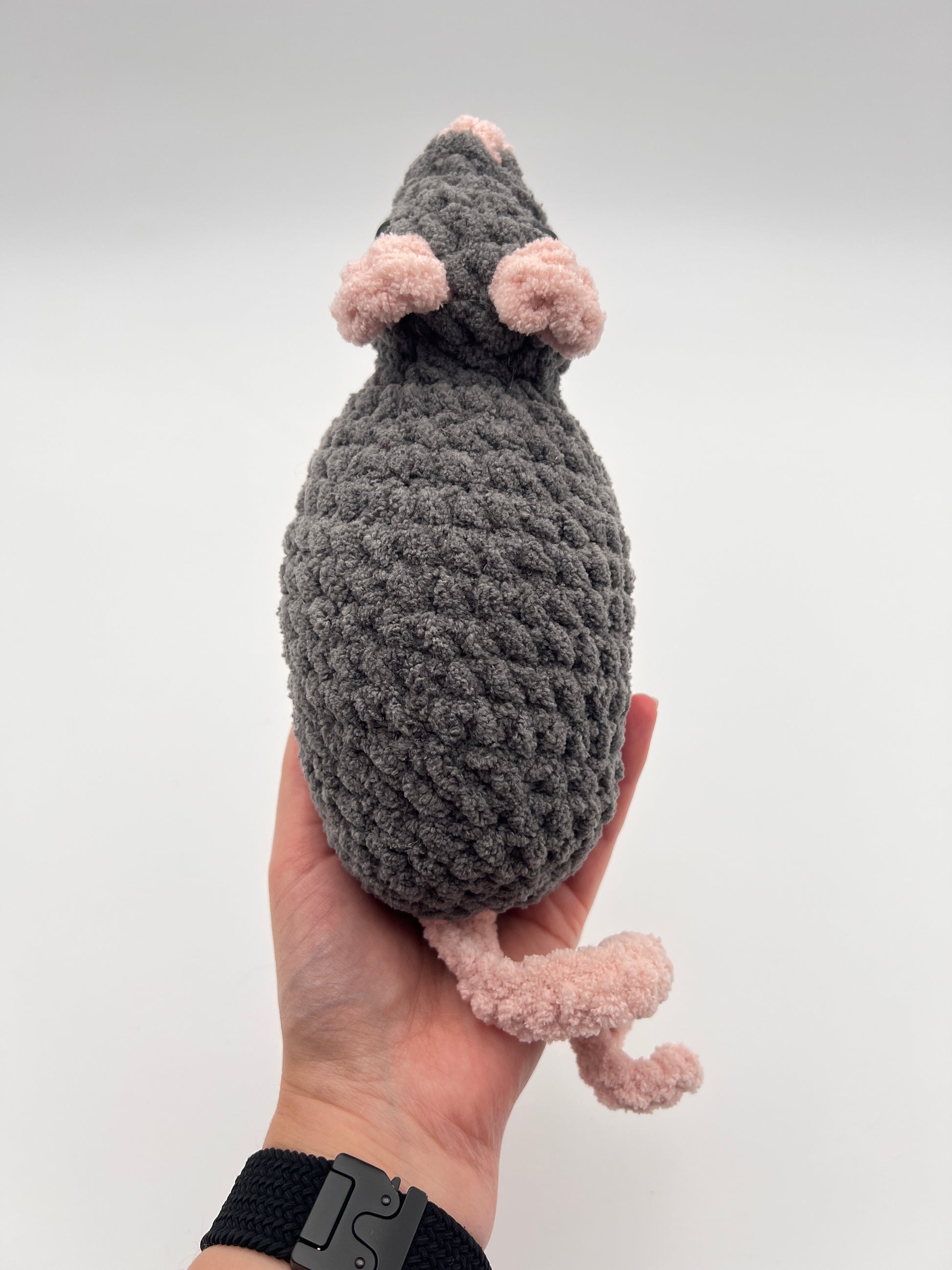 Hand holding a rat stuffed animal toy against a white background