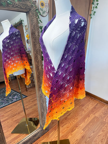 A handmade crochet openwork shawl with a purple-to-orange gradient, displayed on a white mannequin torso in an indoor room with a wooden floor and mirror.