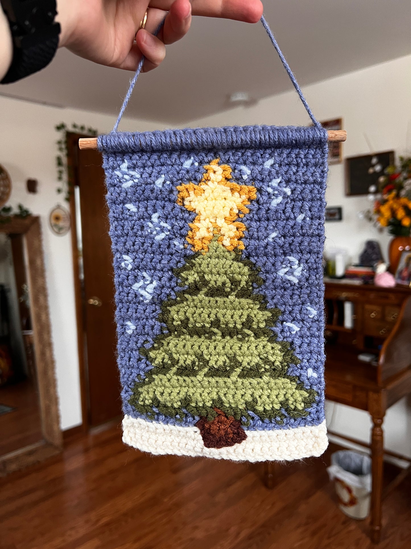 Handmade crochet wall hanging with christmas tree and snow held by a person