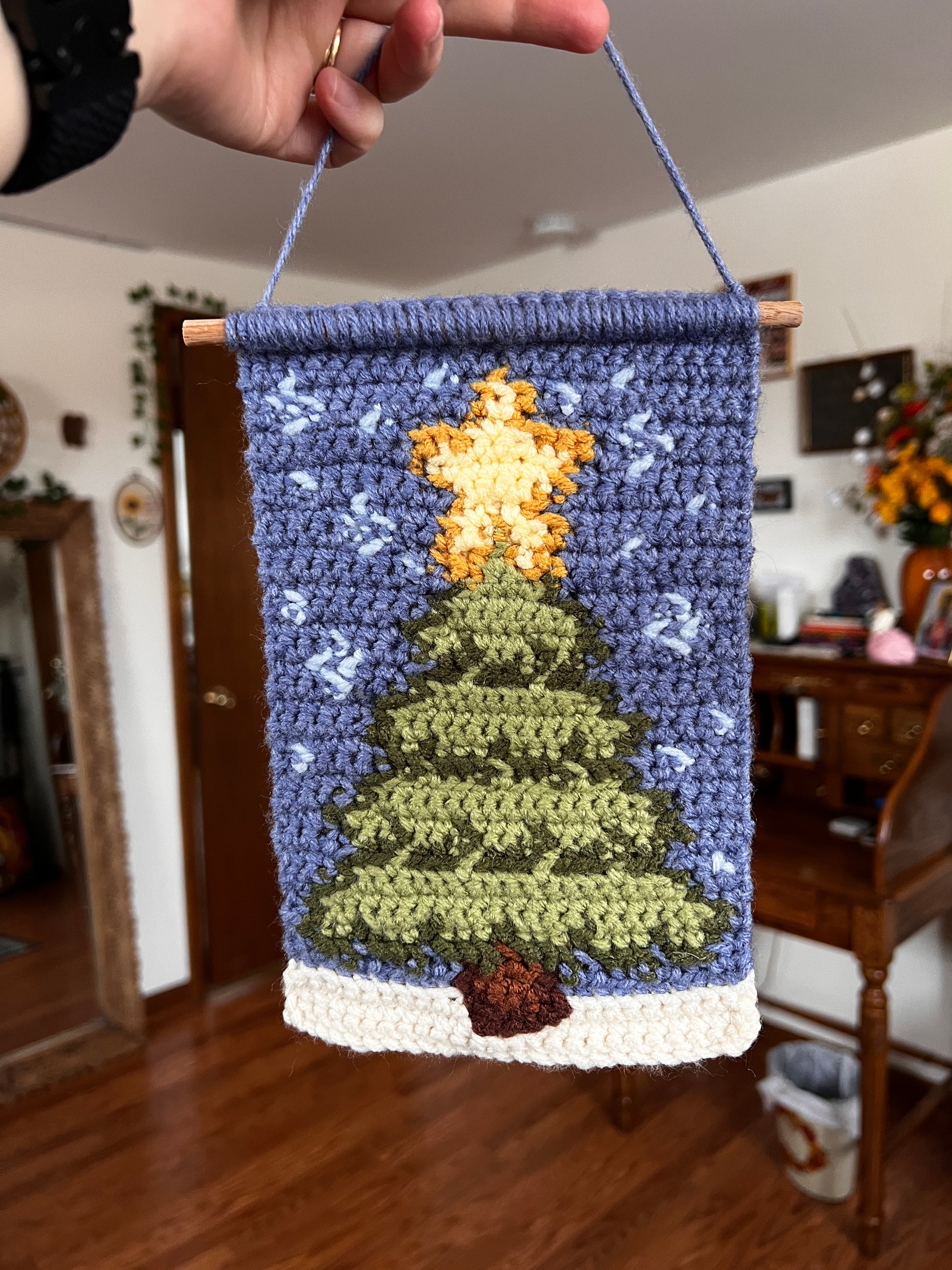 Handmade crochet wall hanging with christmas tree and snow held by a person