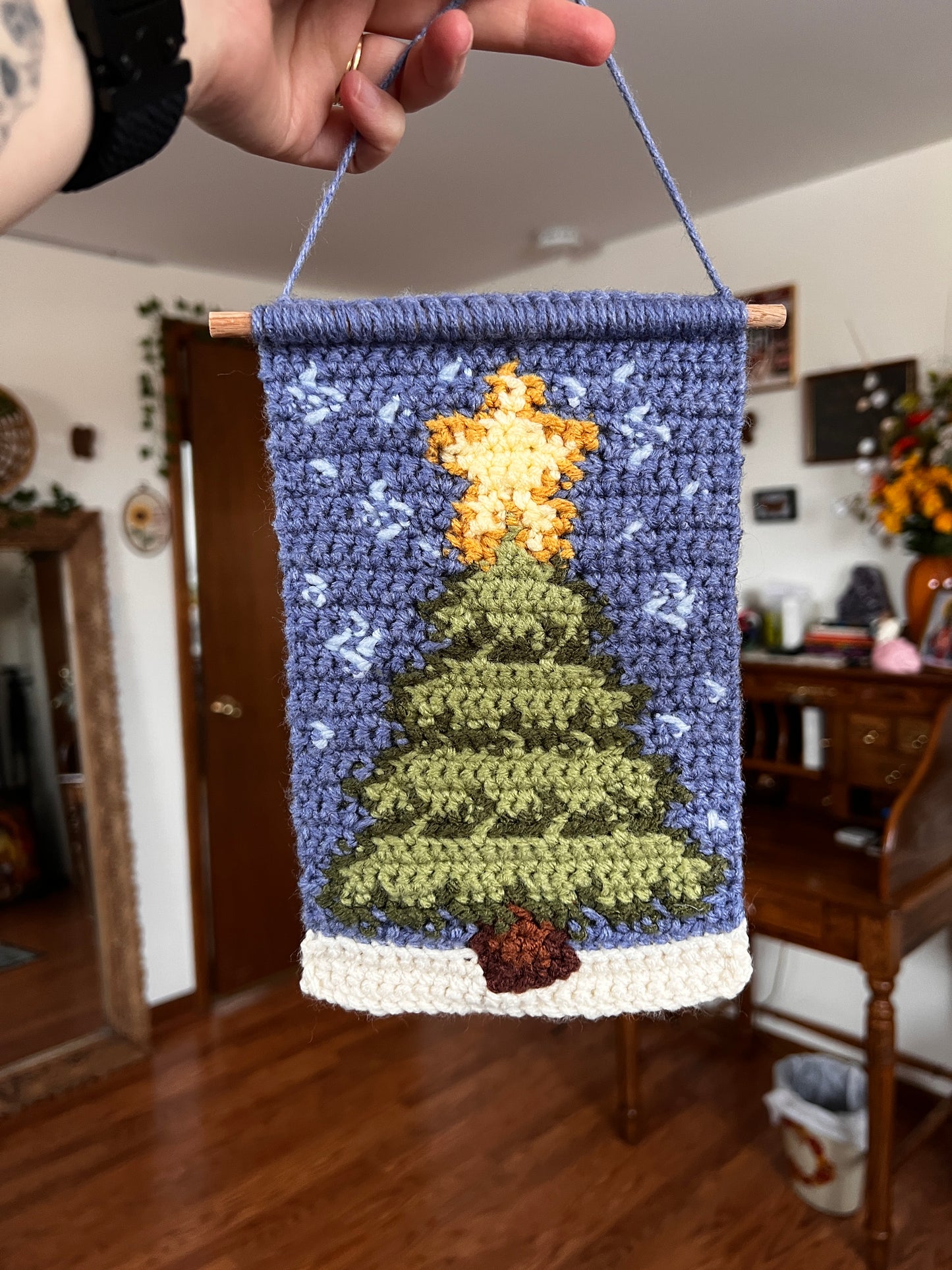 Handmade crochet tapestry with Christmas tree held by a person.
